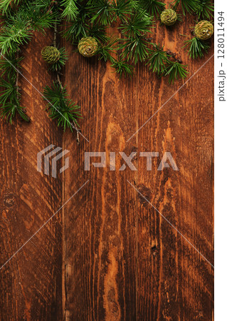 On a brown wooden board lie larch branches with small green cones. Space for text. 128011494