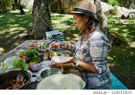 Woman Preparing Ingredients for a Picnic Meal in a Forest Set-Up 128012824