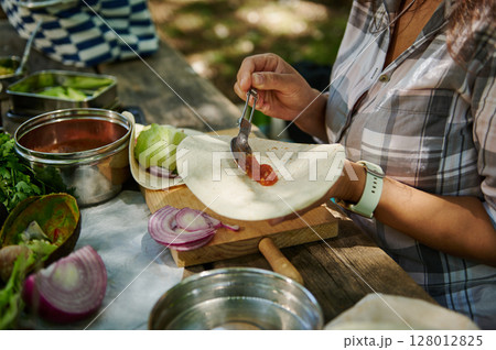 Person Preparing a Fresh Tortilla Meal Outdoors on a Rustic Wooden Table 128012825