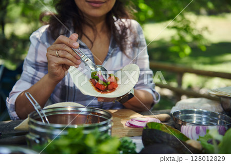 Person Preparing a Fresh Taco Outdoors with Vegetables 128012829