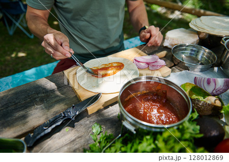 Man Preparing a Burrito with Fresh Ingredients Outdoors on a Wooden Table 128012869
