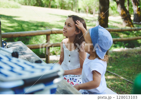 Children Enjoying an Outdoor Picnic in a Park Surrounded by Lush Greenery During a Sunny Day Children Enjoying an Outdoor Picnic in a Park Surrounded by Lush Greenery During a Sunny Day 128013103
