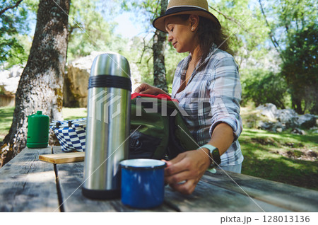 Woman Preparing for a Picnic in a Forest Setting with Camping Gear and Accessories on a Wooden Table Woman Preparing for a Picnic in a Forest Setting with Camping Gear and Accessories on a Wooden Table 128013136