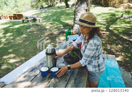 Woman Enjoying Outdoor Picnic Setting on Rustic Table in Nature 128013140