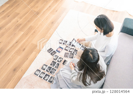 エコー写真を見ながら、赤ちゃんが生まれてくるのが待ち遠しい母と娘 エコー写真を見ながら、赤ちゃんが生まれてくるのが待ち遠しい母と娘 128014564
