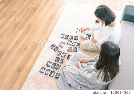 エコー写真を見ながら、赤ちゃんが生まれてくるのが待ち遠しい母と娘 エコー写真を見ながら、赤ちゃんが生まれてくるのが待ち遠しい母と娘 128014565