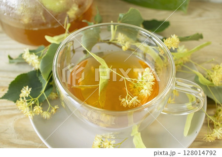Linden tea in a glass cup with fresh linden flowers, on a wooden background. Medicinal herbal tea. Linden tea in a glass cup with fresh linden flowers, on a wooden background. Medicinal herbal tea. 128014792