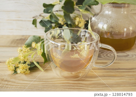 Linden tea in a glass cup with fresh linden flowers, on a wooden background. Medicinal herbal tea. Linden tea in a glass cup with fresh linden flowers, on a wooden background. Medicinal herbal tea. 128014793