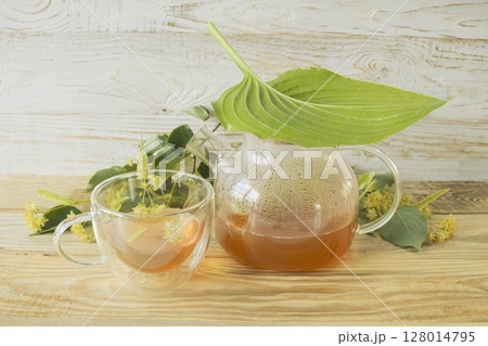 Linden tea in a glass cup with fresh linden flowers, on a wooden background. Medicinal herbal tea. Linden tea in a glass cup with fresh linden flowers, on a wooden background. Medicinal herbal tea. 128014795
