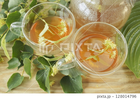 Linden tea in a glass cup with fresh linden flowers, on a wooden background. Medicinal herbal tea. Linden tea in a glass cup with fresh linden flowers, on a wooden background. Medicinal herbal tea. 128014796