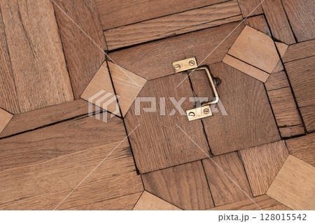 Detailed view of a wooden floor featuring a brass handle and geometric patterns 128015542