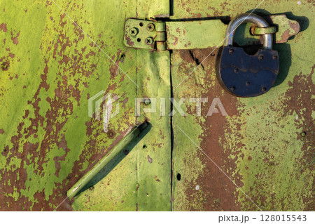 Weathered green painted door featuring a sturdy black padlock Weathered green painted door featuring a sturdy black padlock 128015543