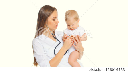 Young woman doctor holding baby and listens to his heart standing on white background Young woman doctor holding baby and listens to his heart standing on white background 128016588