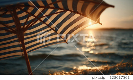 Striped Beach Umbrella at Sunset Over Ocean Waves 128017561