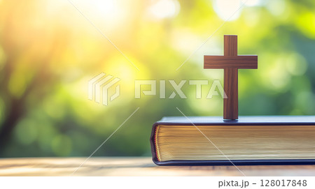 A wooden cross resting on a book in a serene outdoor setting during golden hour light 128017848