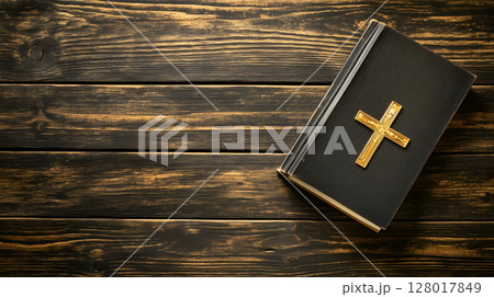A cross placed on a book resting on a wooden surface with ample negative space 128017849