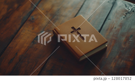 A leather-bound book with a cross invites contemplation on a rustic wooden table 128017852