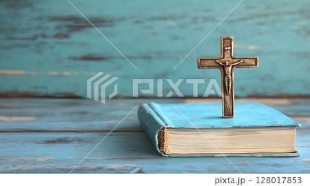 A cross resting on a book against a rustic wooden background with ample negative space 128017853