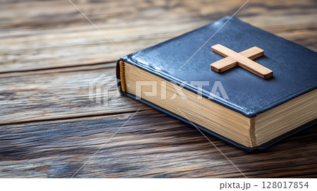 A wooden cross resting on a closed book against a rustic wooden background with ample space 128017854