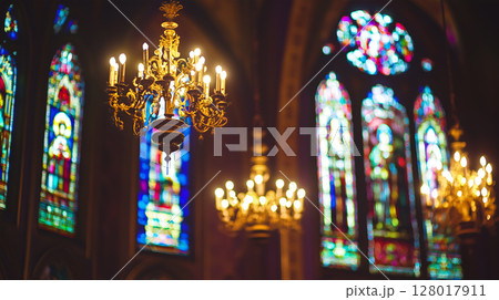 Elegant chandeliers illuminate stained glass windows in a historic church interior 128017911
