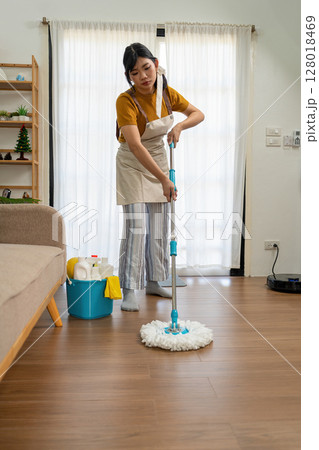Young modern Asian woman doing house cleaning at home. Confident and independent homemaker maintaining a clean, stylish living space. Young modern Asian woman doing house cleaning at home. Confident and independent homemaker maintaining a clean, stylish living space. 128018469