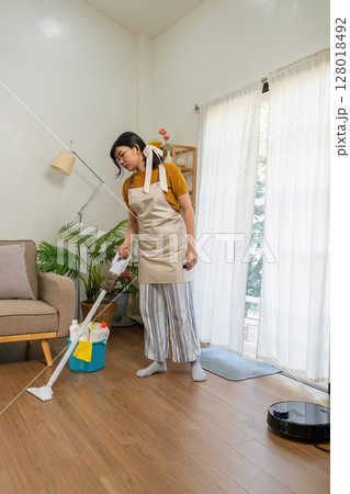 Young modern Asian woman doing house cleaning at home. Confident and independent homemaker maintaining a clean, stylish living space. 128018492