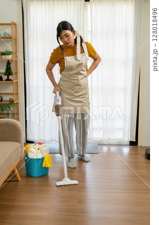 Young modern Asian woman doing house cleaning at home. Confident and independent homemaker maintaining a clean, stylish living space. Young modern Asian woman doing house cleaning at home. Confident and independent homemaker maintaining a clean, stylish living space. 128018496