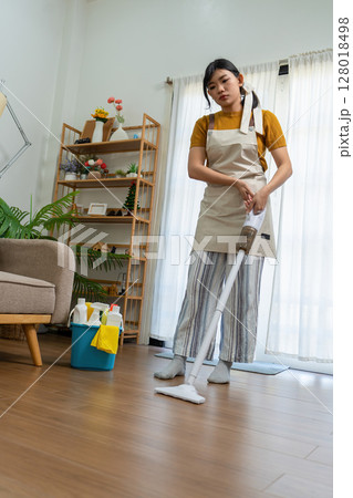 Young modern Asian woman doing house cleaning at home. Confident and independent homemaker maintaining a clean, stylish living space. Young modern Asian woman doing house cleaning at home. Confident and independent homemaker maintaining a clean, stylish living space. 128018498