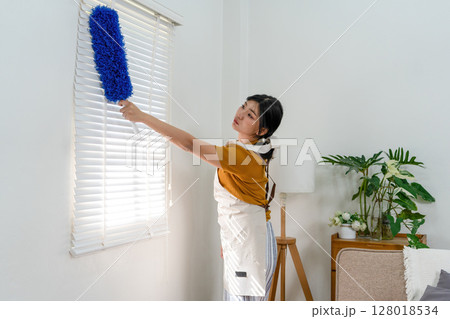 Young modern Asian woman doing house cleaning at home. Confident and independent homemaker maintaining a clean, stylish living space. Young modern Asian woman doing house cleaning at home. Confident and independent homemaker maintaining a clean, stylish living space. 128018534