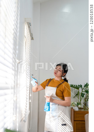 Young modern Asian woman doing house cleaning at home. Confident and independent homemaker maintaining a clean, stylish living space. 128018538