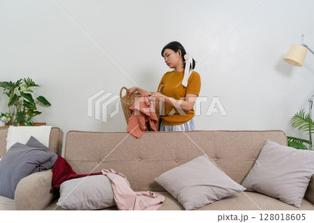 Young modern Asian woman doing house cleaning at home. Confident and independent homemaker maintaining a clean, stylish living space. Young modern Asian woman doing house cleaning at home. Confident and independent homemaker maintaining a clean, stylish living space. 128018605