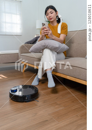 Young modern Asian woman doing house cleaning at home. Confident and independent homemaker maintaining a clean, stylish living space. Young modern Asian woman doing house cleaning at home. Confident and independent homemaker maintaining a clean, stylish living space. 128018611