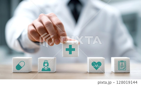 Doctor arranges white blocks with medical symbols, including cross, pill, nurse, heart, and clipboard, symbolizing healthcare concepts 128019144