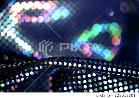 Holographic shiny spots and dots bokeh on fabric for a futuristic disco background Holographic shiny spots and dots bokeh on fabric for a futuristic disco background 128019801