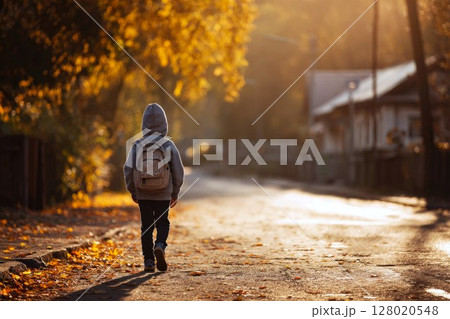 Little boy with backpack on his shoulders walking to school on autumn street, back to school concept, schoolboy in a hurry to study 128020548