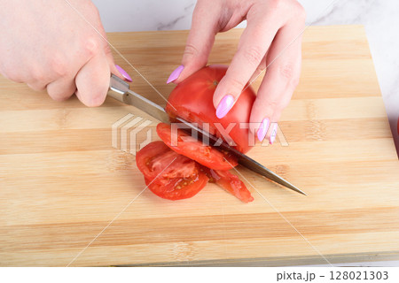 Cutting a tomato into pieces with a knife. 128021303