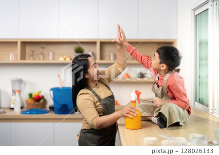 Family Bonding During Cleaning. Mother and son share a high-five while tidying up the kitchen. Family Bonding During Cleaning. Mother and son share a high-five while tidying up the kitchen. 128026133
