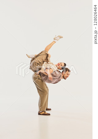 Dynamic retro dance performance with couple in vintage attire and acrobatic pose on neutral backdrop Dynamic retro dance performance with couple in vintage attire and acrobatic pose on neutral backdrop 128026464