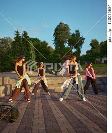 Street dance group performing energetic routine in urban park setting Street dance group performing energetic routine in urban park setting 128026684