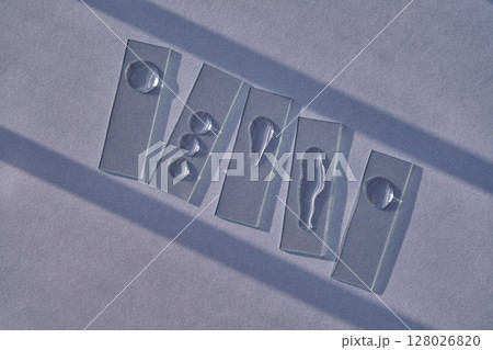 Samples of serum or micellar water on slides on a blue background with streaks of shadows. Samples of serum or micellar water on slides on a blue background with streaks of shadows. 128026820