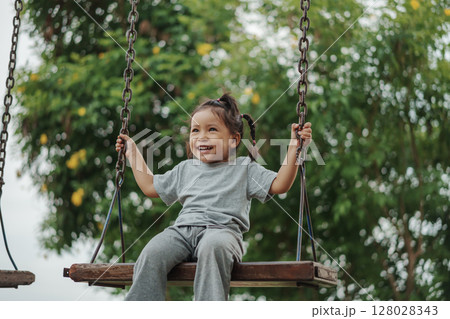 cheerful toddler girl playing on wooden swing at playground 128028343