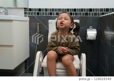 toddler girl sitting on toilet at home and suffering from stomachache and constipation 128028349