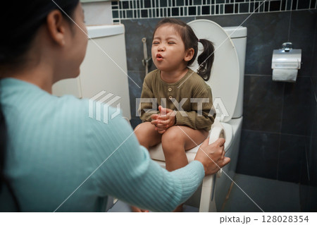 mother is helping toddler girl use the toilet. potty training and learning in bathroom 128028354