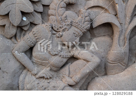 Detailed close-up of traditional Balinese stone carving depicting a figure and foliage 128029188