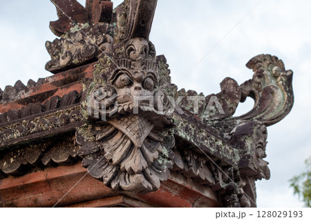 Ancient stone carving detail on a traditional temple roof against a cloudy sky 128029193