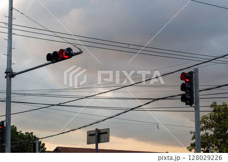 Red traffic lights against a cloudy sky with a complex network of overhead wires. 128029226