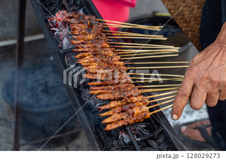Hand Turning Delicious Marinated Chicken Satay on a Traditional Grill 128029273