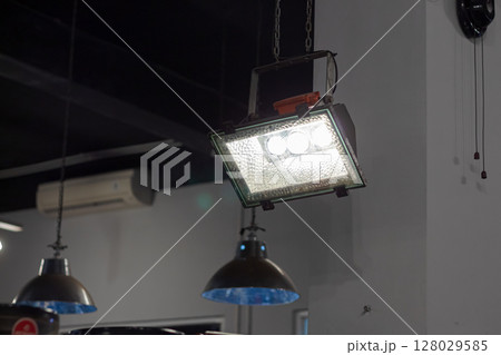 Bright industrial floodlight fixture hanging from the ceiling indoors 128029585