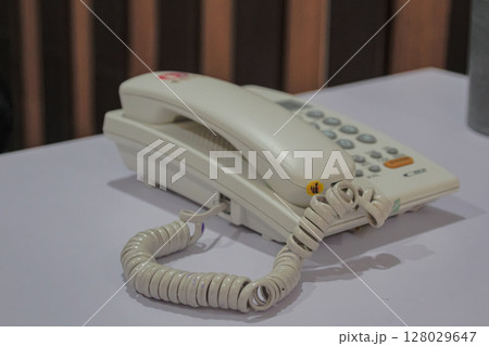 Classic white landline telephone with curly cord resting on a table surface Classic white landline telephone with curly cord resting on a table surface 128029647