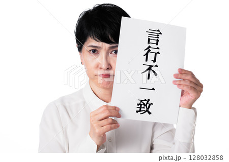言行不一致と書かれた紙を持ち不満げな白いシャツを着た中年女性 言行不一致と書かれた紙を持ち不満げな白いシャツを着た中年女性 128032858